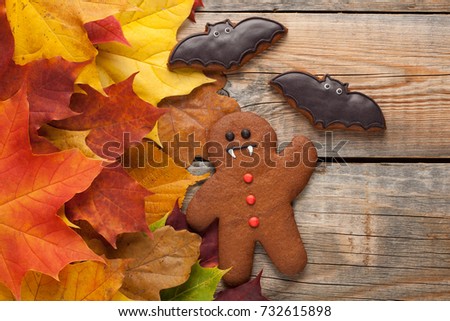 Homemade biscuits in the form of gingerbread men vampire for Halloween. Autumn maple leaves on old wooden background. Top view.