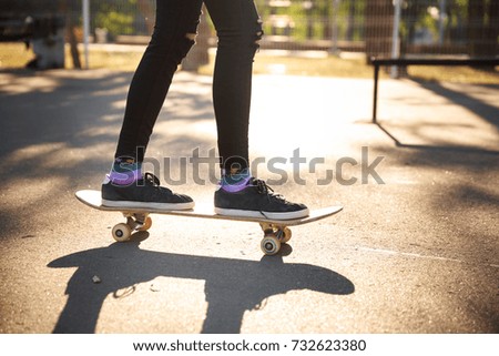 The legs of a skateboarder girl in sneakers do a trick on a skateboard.