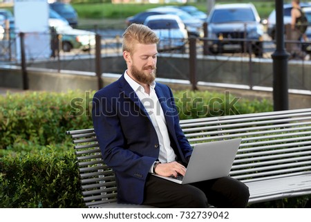 Handsome young man with laptop on bench, outdoors