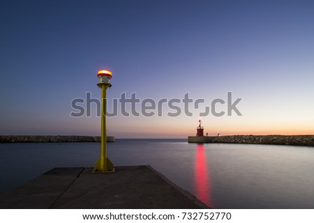 Seascape of a small lighthouse with his red reflections on the sea at sunset. Some people are fishing under the starry sky. Photo taken at sunset in Sabaudia beach, Italy