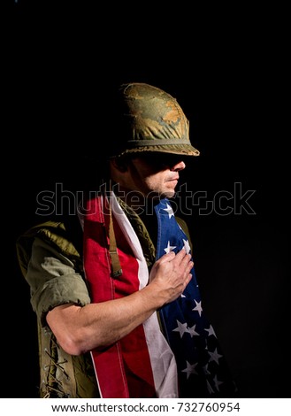 Patriotic US Marine (Vietnam War) with the American flag around his shoulders, standing against a black background.