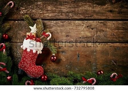 Festive Christmas border with colorful patterned red boot or stocking filled with decorations, and a gift on rustic wood background with pine and candy cane border