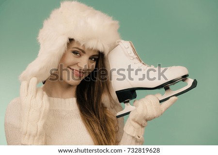 Winter sport activity concept. Woman wearing furry warm hat holding ice skate, blue background studio shot.