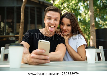 Portrait of a funny young couple taking selfie while sitting together at the cafe outdoors