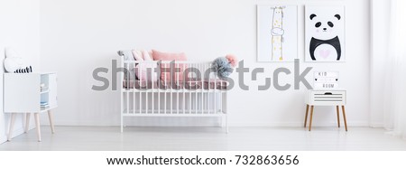 White wooden crib with cute pillows and tulle pompoms in the room with two posters with panda and giraffe