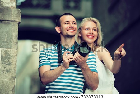 joyful young excited couple looking curious and taking pictures outdoors in trip. Focus on man
