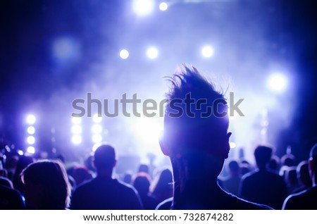 silhouettes of concert crowd and mohawk punk hair style in front of bright stage lights