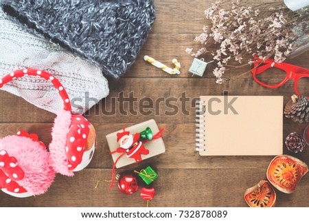 Creative flat lay of Christmas ornaments, winter accessories and craft notebook on wood background, Top view