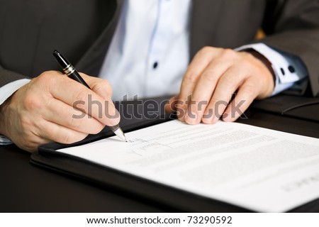 Businessman in dark suit and blue shirt sitting at office desk signing a contract with shallow focus on signature. Royalty-Free Stock Photo #73290592