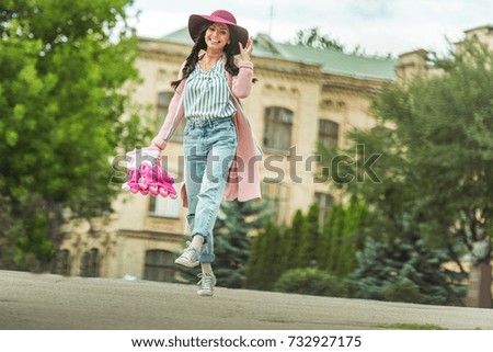 low angle view of cheerful young woman holding roller skates and smiling at camera