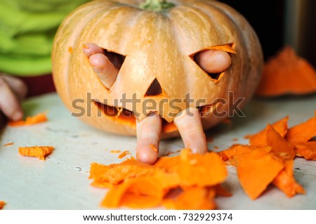 Process of making Jack-o-lantern. Funny picture of Halloween pumpkin monster face with male fingers. Selective focus and bokeh.