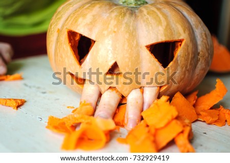Process of making Jack-o-lantern. Funny picture of Halloween pumpkin monster face with male fingers. Selective focus and bokeh.
