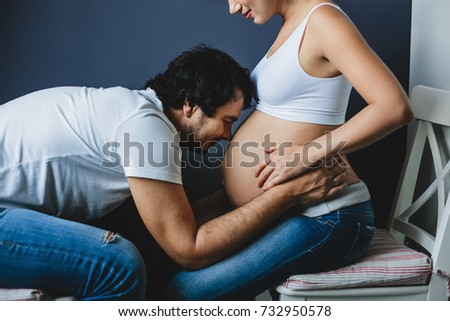Man leans to woman's pregnant belly sitting with her on the chairs
