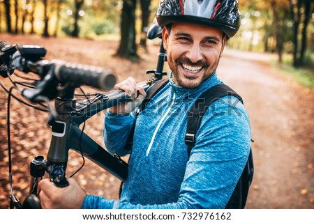 Young pretty athletic man standing with bicycle in autumn park. Royalty-Free Stock Photo #732976162