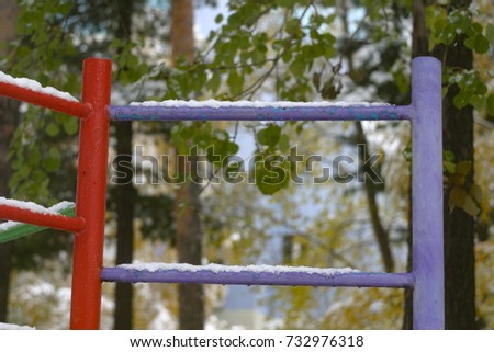 Red, purple ladder stair in the playground, covered with white snow, fallen yellow leaves, green foliage. The first snow in autumn, in October. Autumn and winter background