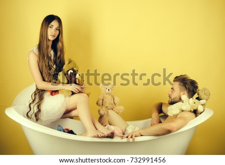 Love and romance. Man in bathtub near girl with long hair. Woman in dress and guy with toy bear. Boyfriend and girlfriend relax on yellow background. Couple in love of man and woman in bath.