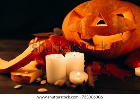Shiny candles, cinnamon and fallen leaves stand before scarry Halloween pumpkin
