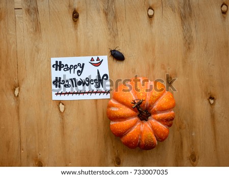 A pumpkin and Happy Halloween text on a note on wooden table with a beetle