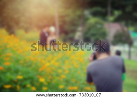 Blurred background wedding photographer in action. Photographey taking photographs of groom and bride in beautiful garden. Blurred background behind the scenes concept.