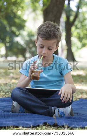 little cute boy of school age uses a digital tablet while lying on the grass. He looks at his favorite video clips. Digital generation next