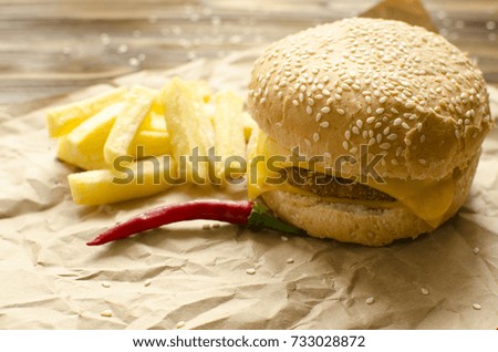 Cheeseburger with fried potatoes and chili  on a  craft paper on wooden background with space for text