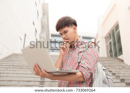 Young man sitting with laptop outside the university building 