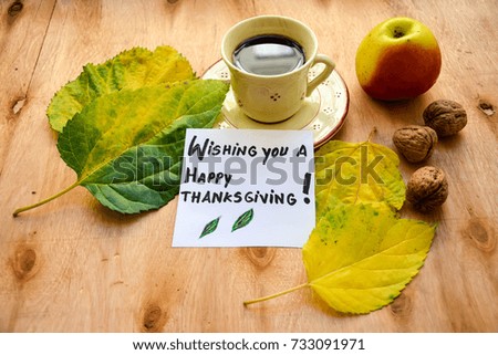 A cup of coffee ,an apple , autumn leaves and wishing you a Happy Thanksgiving text on a note on wooden table