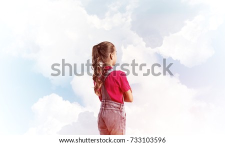 Little cute girl in overalls against sky background dreaming about future Royalty-Free Stock Photo #733103596
