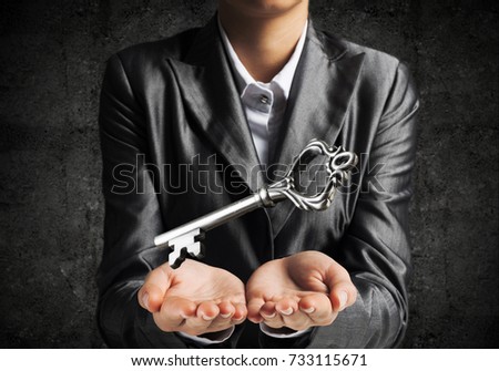 Cropped image of businessman in suit keeping big key in hands with dark wall on background.
