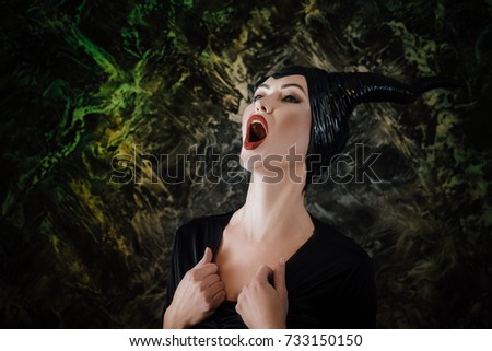 beautiful woman dressed as a fairy witch in raincoat and with horns screams in pain. image for Halloween