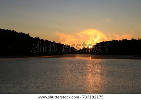 Sunset (or sunrise) view with magnificently colored sky over a body of water with landscape and trees silhouetted at the horizon.