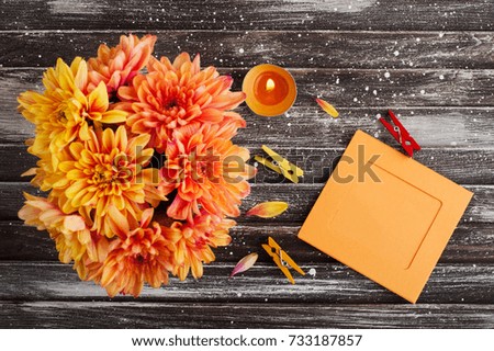 Autumn background with orange chrysanthemum on rustic wooden table. Empty photo frame and lit candle