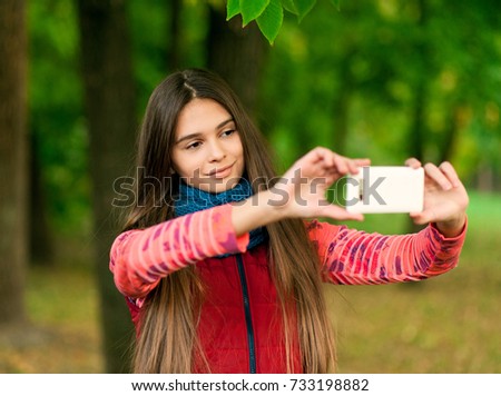 beautiful young girl taking selfie with smartphone in autumn leaves. Season, technology and people concept