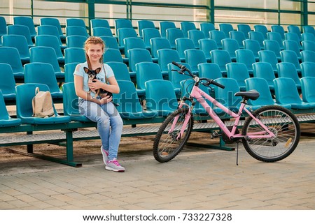smiling girl relaxing with dog Chihuahua. Sporty kid posing with a Bicycle. girl in the blue seats of the stadium.