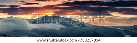 Panoramic view of winter mountains at sunrise.  Landscape with foggy hills  and trees covered with rime. Dramatic cloudy over sky. 