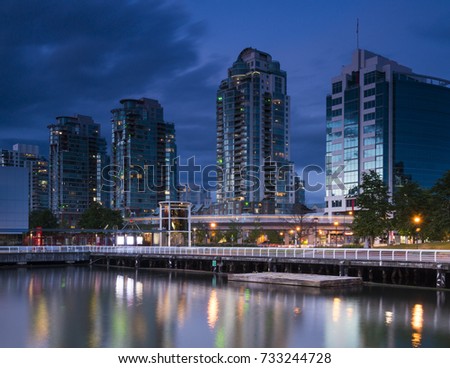 Vancouver Nighttime shot with skytrain moving in front of 4 buildings that overlook False Creek