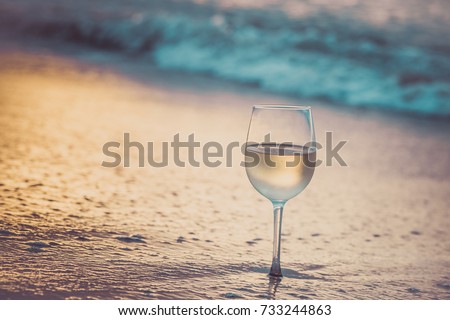 A glass  of white wine on the beach at sunset. Travel vacations concept.