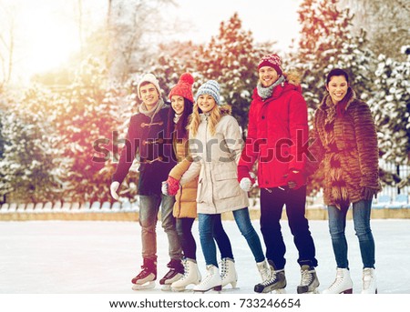 people, winter, friendship, sport and leisure concept - happy friends ice skating and holding hands on rink outdoors
