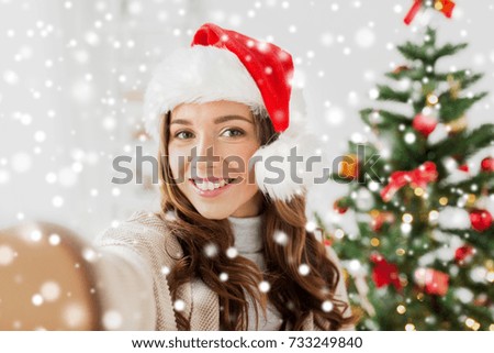 winter holidays and people concept - happy young woman or teenage girl in santa hat over christmas tree taking selfie over snow