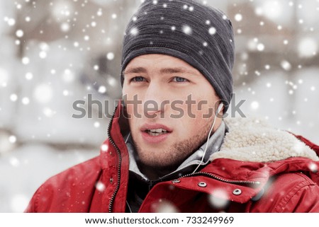 people, christmas, winter and season concept - close up of man in jacket and hat with earphones listening to music outdoors