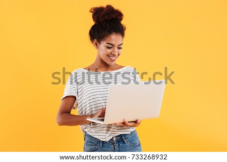 Young african positive cool lady with curly hair using laptop and smiling isolated over yellow