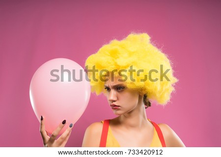 girl with yellow wig evil looking at pink balloon