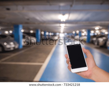 Hand holding mobile phone with blurred image of indoor car parking lot, Internet, Social media