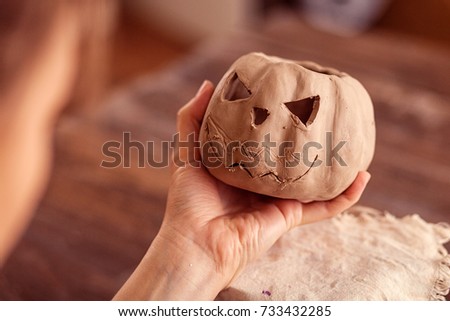 A close-up of a female potter holding in his hand a small pumpkin made of clay with a jack's face against the background of a wooden table