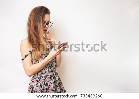girl in dress looks into phone and looks surprised