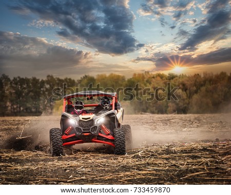 Racing quad bike with two pilots in helmets on the field. Sunset landscape. The concept of speed and freedom.