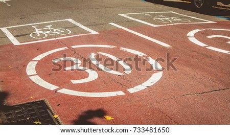white paint on a red road indicating the presence of a bicycle and forbidden to exceed the speed of 30