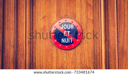 on a varnished wooden door of a building, a sign forbidding parking where it is written in French - day and night