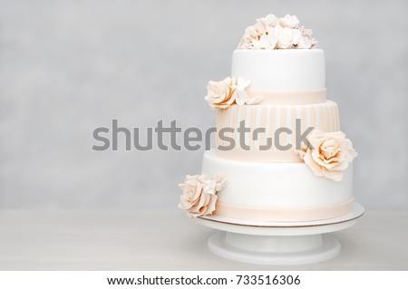 Three-tiered white wedding cake decorated with flowers from mastic on a white wooden table. Picture for a menu or a confectionery catalog with copy space.
