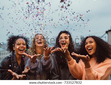 Happy friends standing on a terrace. Group of young women throwing confetti. Royalty-Free Stock Photo #733527832